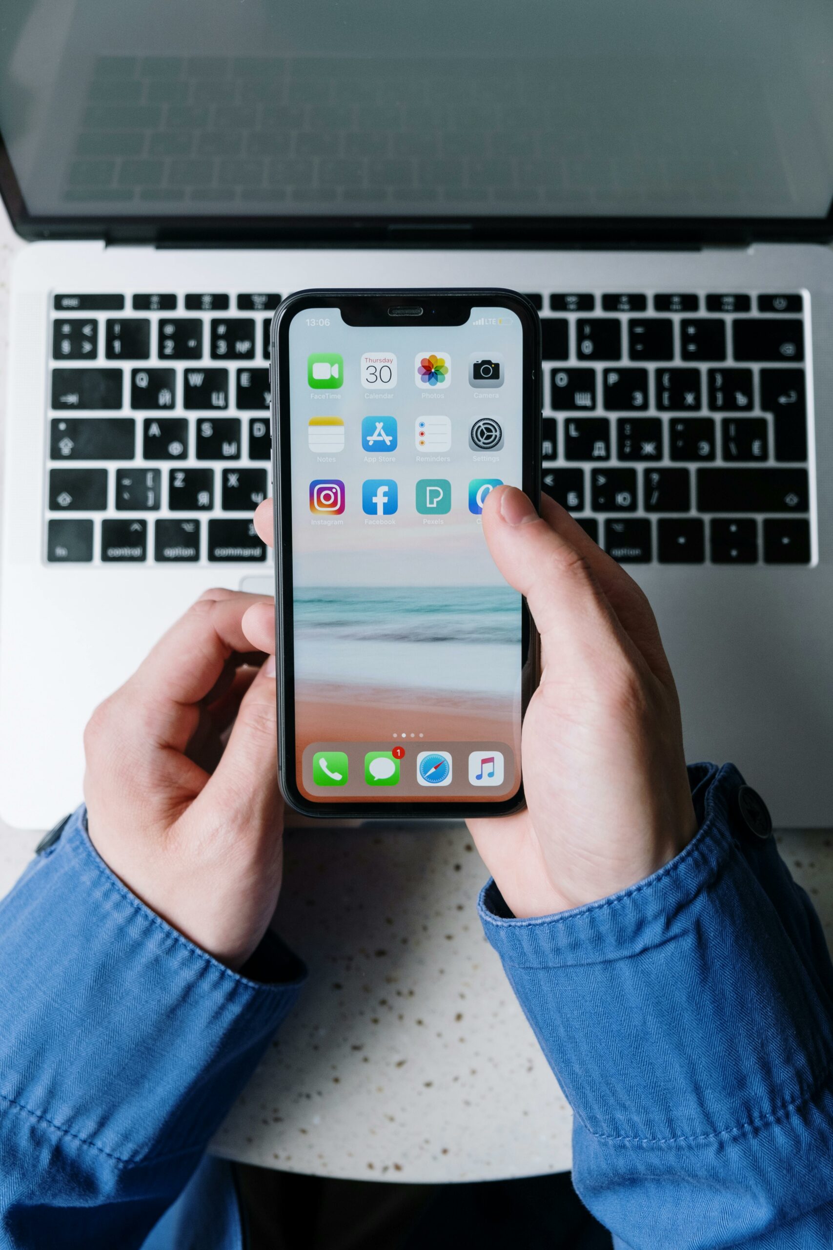 Hands holding a smartphone with apps in front of a laptop, symbolizing digital tools for data and analytics.