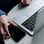A hand placing a smartphone next to a laptop on a desk, representing integration of digital tools and analytics.