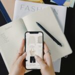 Hands holding a smartphone with fashion shopping items, notebook and moodboard in background – example of SEO and digital marketing visuals.